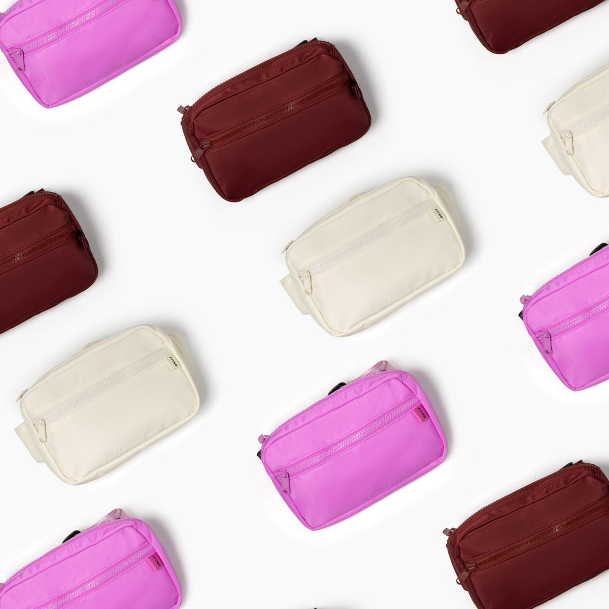 A flat-lay arrangement of multiple zippered pouches in bright pink, cream, and burgundy on a clean white background.