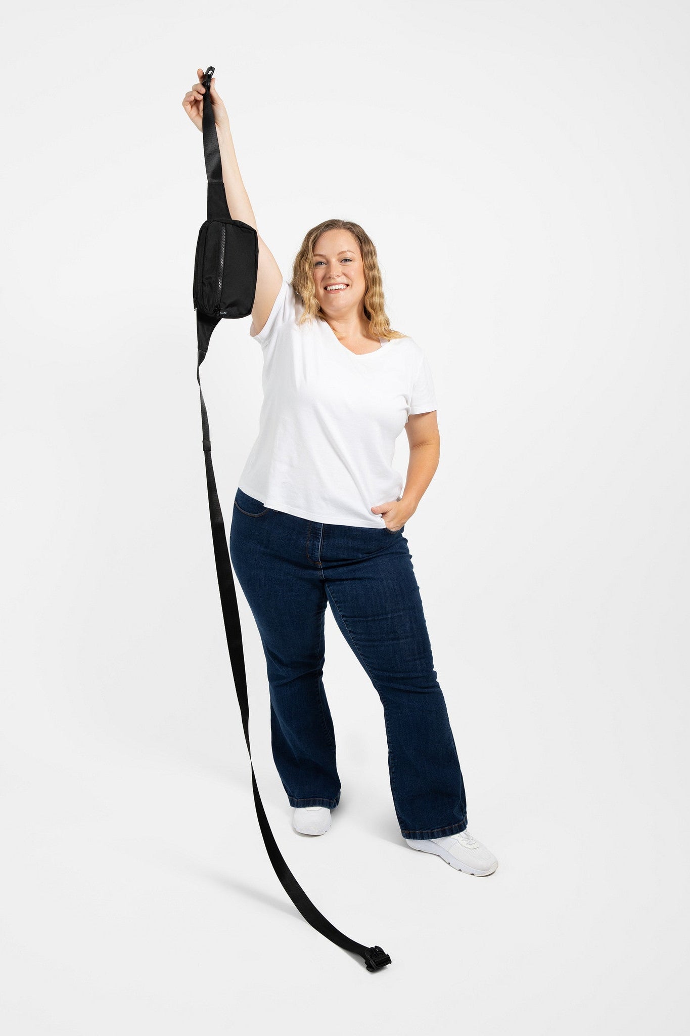 Person holding a long black strap from a plus size belt bag against a white background