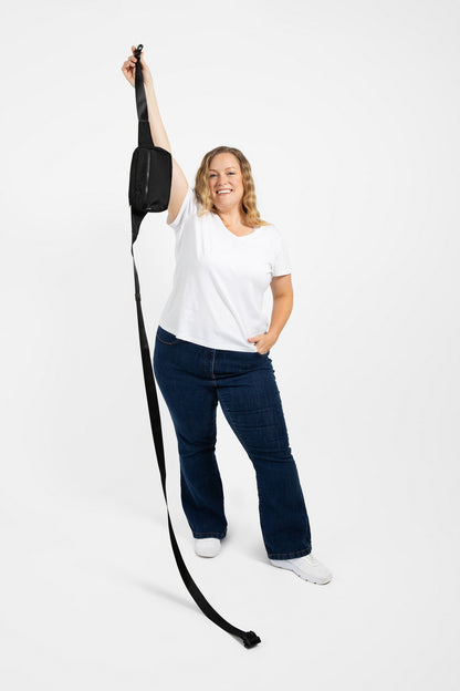 Person holding a long black strap from a plus size belt bag against a white background